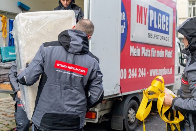 Wiener Möbelpacker heben schweren Gegenstand in Umzugstransporter